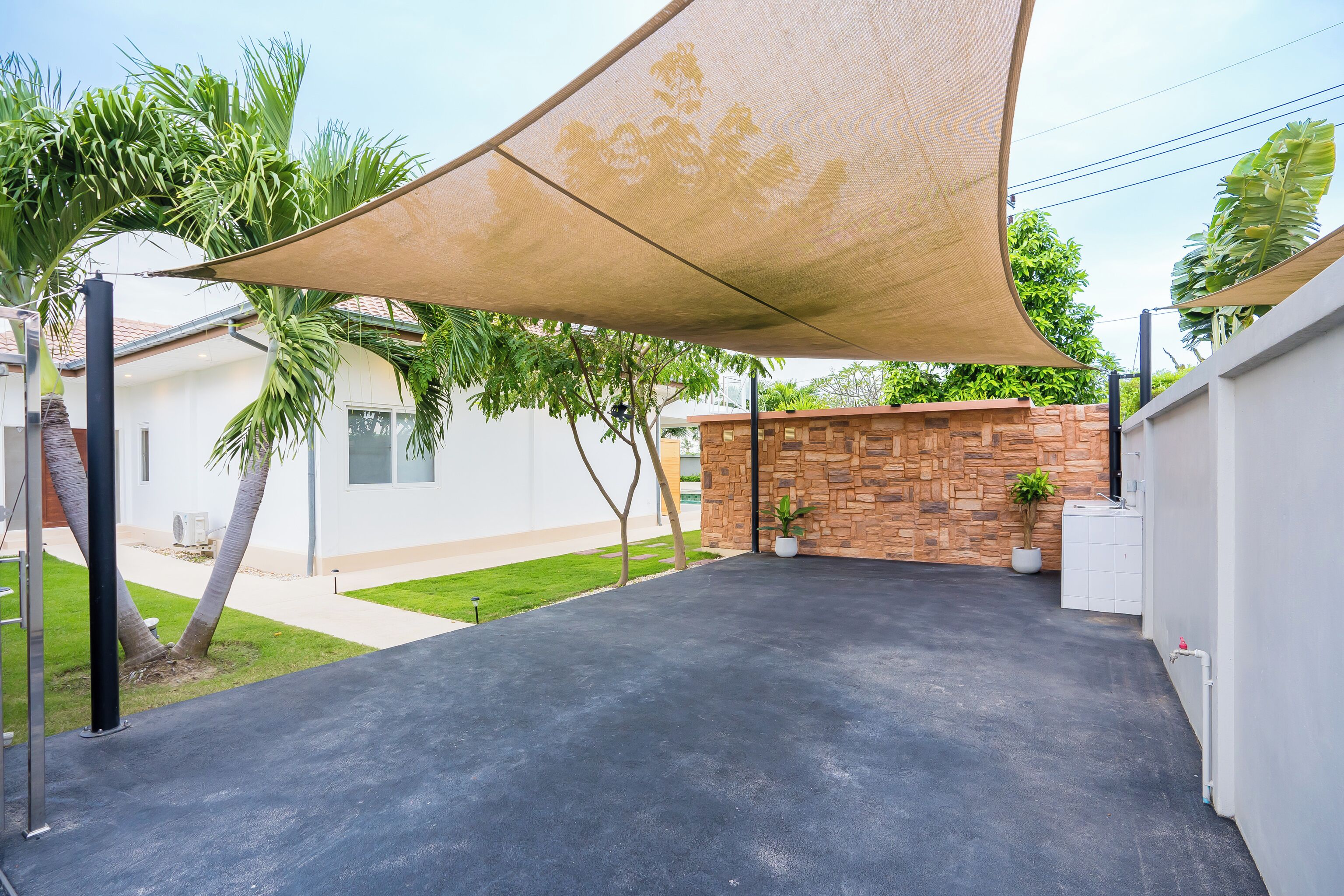 A covered patio with a black surface, surrounded by a white wall and a stone wall with potted plants.