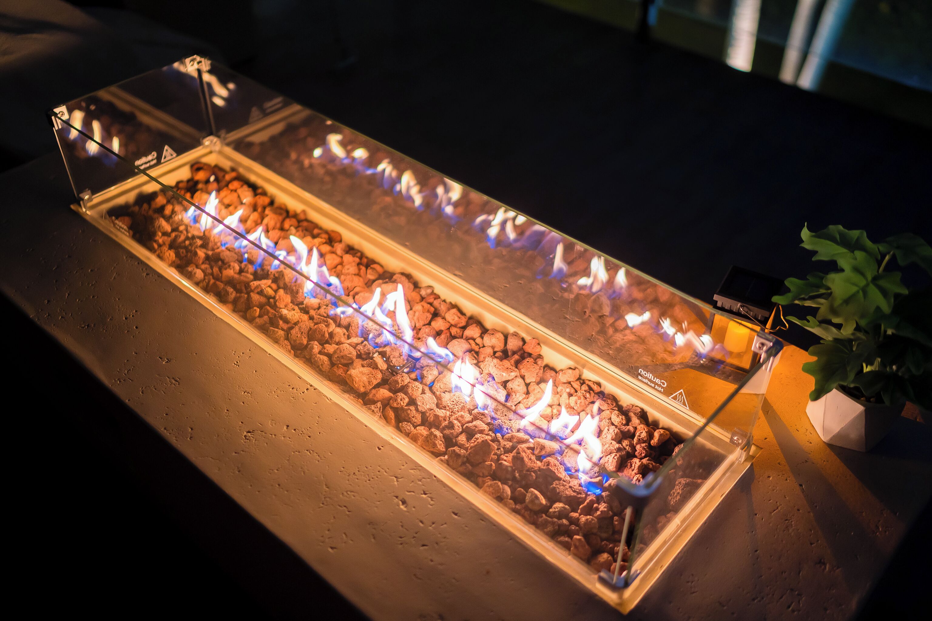 Un foyer rectangulaire doté d’une enceinte en verre, entouré de roches et illuminé par des flammes.