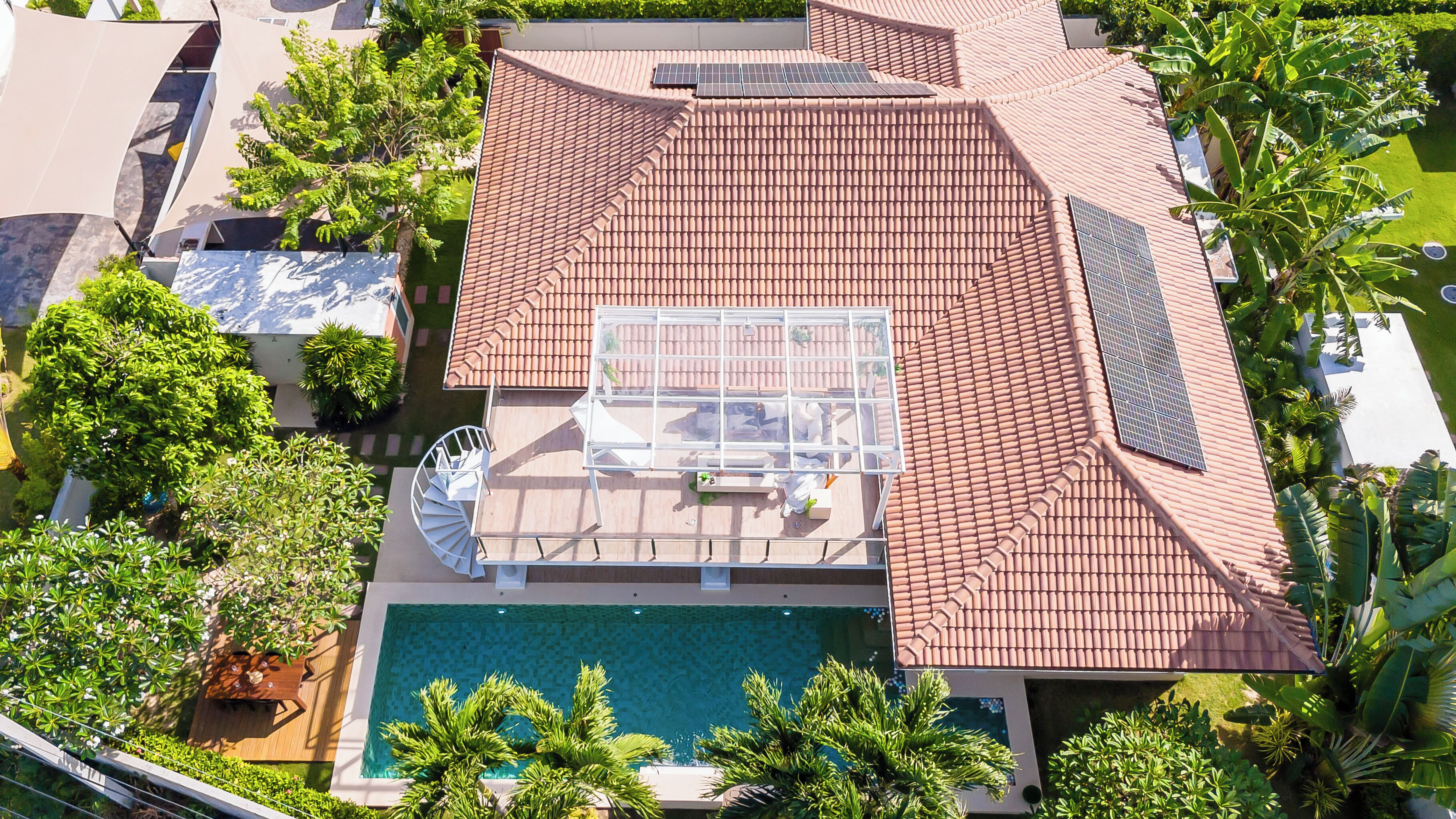 An aerial view of a residential property with a swimming pool, a covered patio, and a solar panel array.