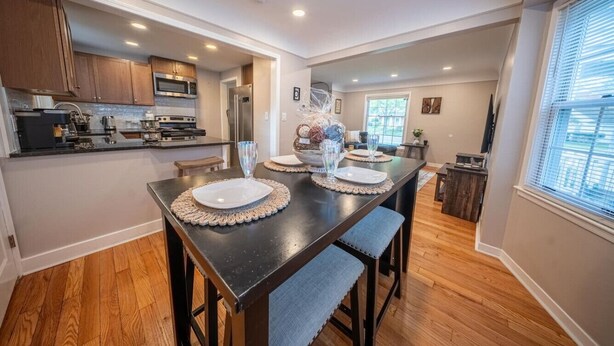 Una cocina moderna con armarios de madera, electrodomésticos de acero inoxidable y una zona de comedor con mesa de madera oscura y sillas tapizadas en azul.