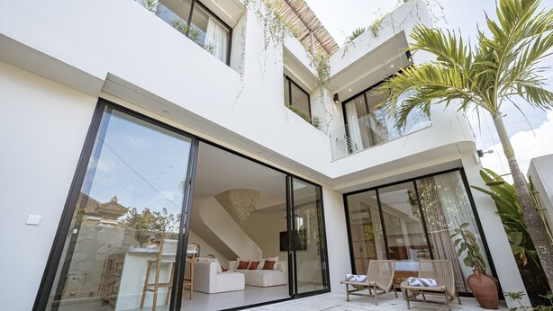 Una casa moderna con un gran ventanal, una piscina y un patio con sillas de descanso.