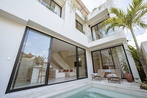 A modern house with a large glass door, a pool, and a patio area with lounge chairs.