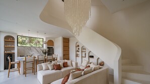 Una sala moderna con sofá, mesa de comedor y sillas. Una escalera conduce a otro nivel.