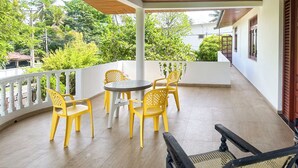 Un espace extérieur abrité, doté d’un plafond en bois, de murs blancs et d’une rambarde blanche. On y trouve des chaises en plastique jaunes et une petite table ronde.