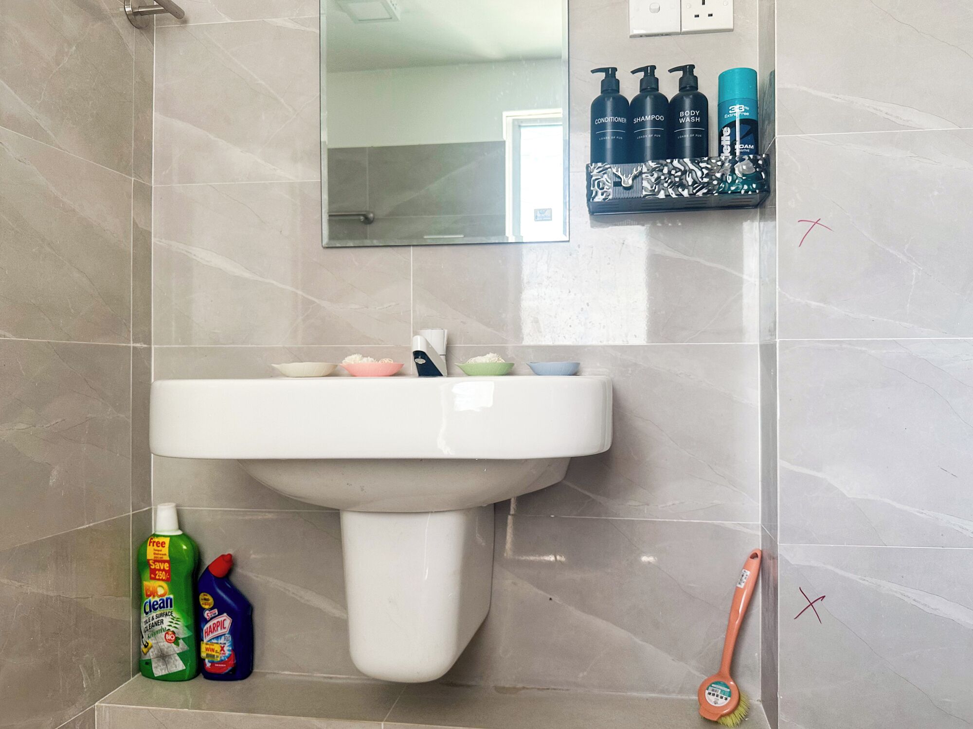 Un bagno con un lavandino bianco, uno specchio sopra e articoli da toilette a parete.