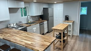 A modern kitchen with a wooden island, stainless steel appliances, and a small wooden table. - Tranquil cabin with WiFi in charming Au Train. (Au Train)