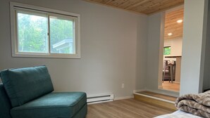 A room with a green sofa, a bed with a white cover, a window, and a view of an outdoor area with a wooden ceiling. - Tranquil cabin with WiFi in charming Au Train. (Au Train)