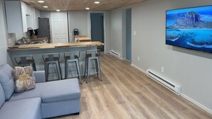 A modern kitchen with a wooden ceiling, a bar area with stools, and a large flat-screen TV mounted on the wall. - Tranquil cabin with WiFi in charming Au Train. (Au Train)