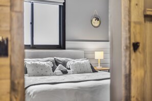 Une chambre à coucher avec un lit, des oreillers, une table de chevet avec une lampe, une fenêtre et un élément décoratif fixé au mur.