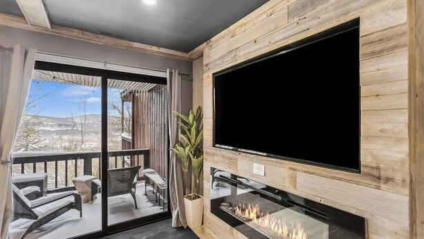 Un salon moderne doté d’une cheminée, d’un grand téléviseur et d’un balcon avec un espace salon extérieur.