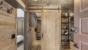 Un intérieur en bois avec une porte coulissante, un lit et une étagère où sont posées des bouteilles et des verres.