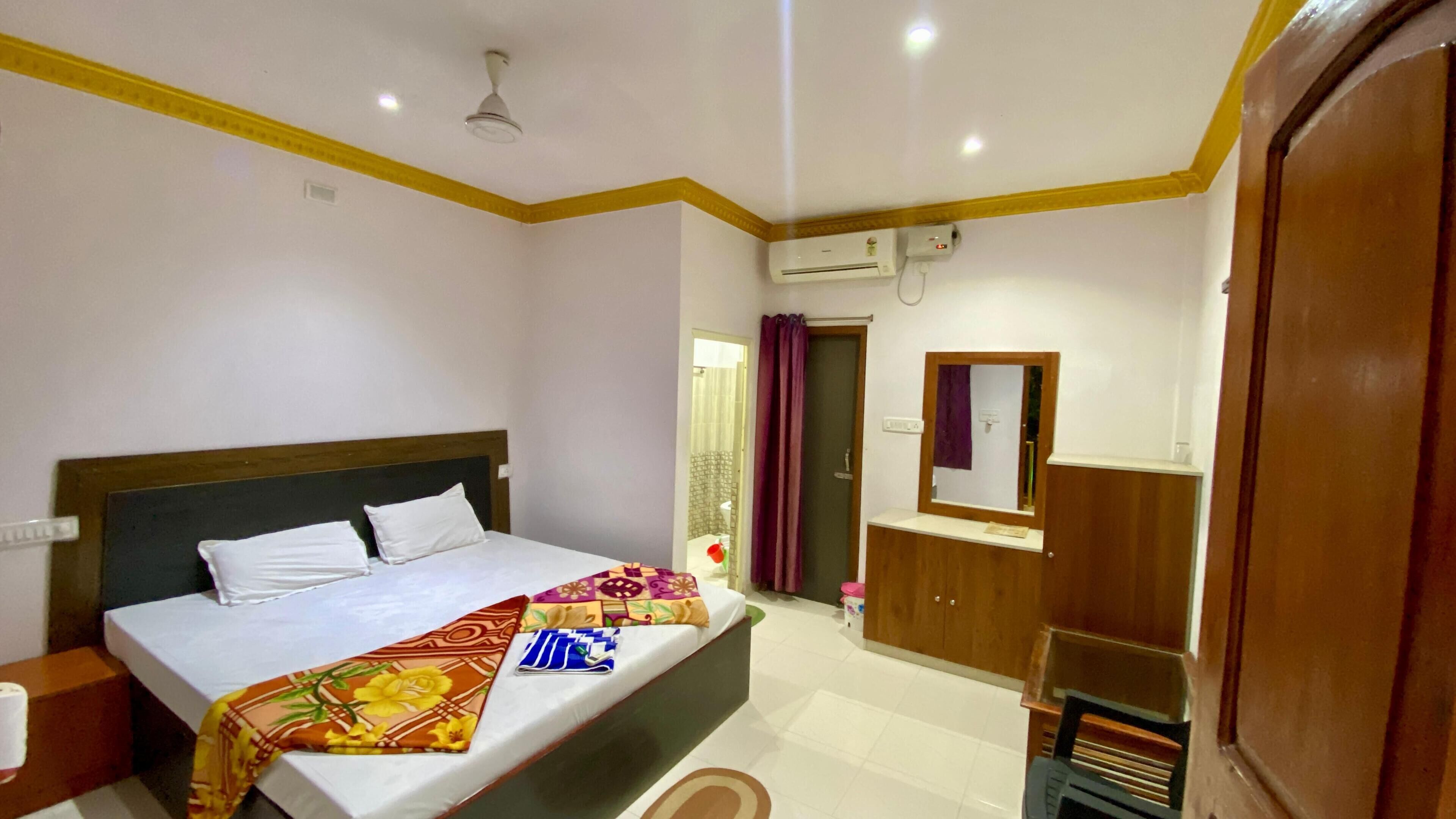 A bedroom with a bed, a bedside table, an air conditioning unit, a mirror, and a wardrobe.