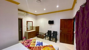 Une chambre à coucher comprenant un lit, un bureau, deux chaises, un miroir, une télévision et une porte.
