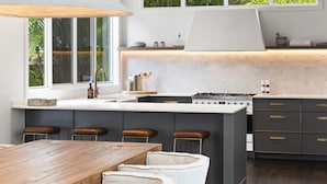 Een moderne keuken met een groot eiland, barkrukken en uitzicht op groen.