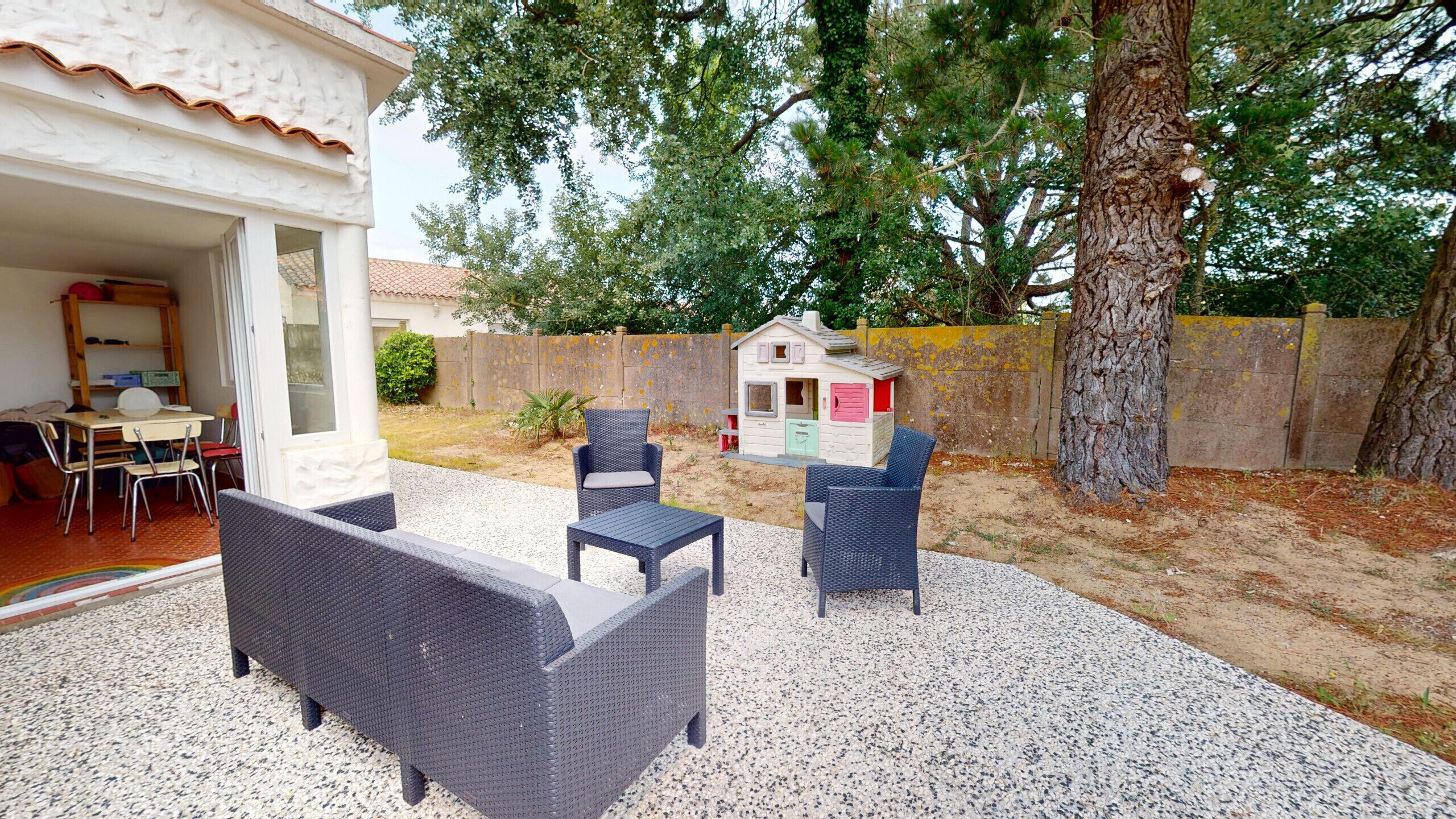 Une terrasse extérieure avec des meubles en osier, une maisonnette pour enfants et un sol en gravier.