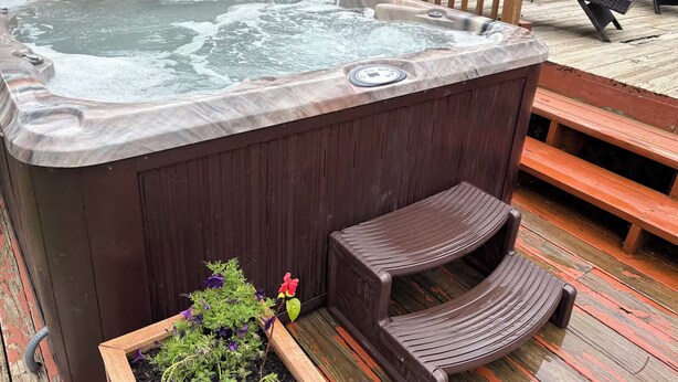 Un bain à remous sur une terrasse en bois, avec un banc en bois et un jardinier décoré de fleurs.