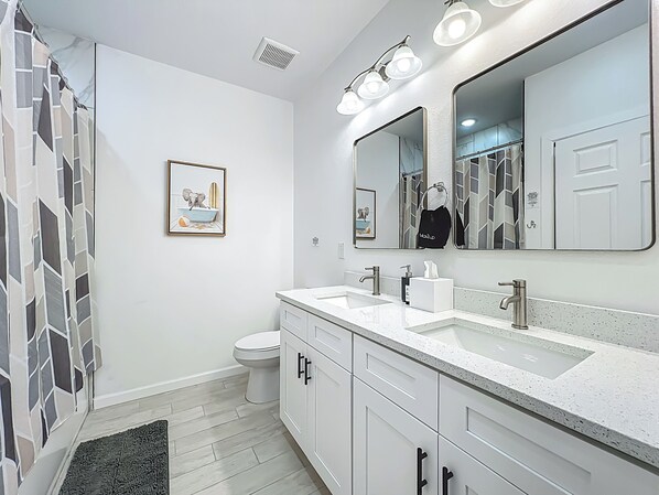 A modern bathroom with a white sink, two mirrors, a toilet, and a shower curtain.
