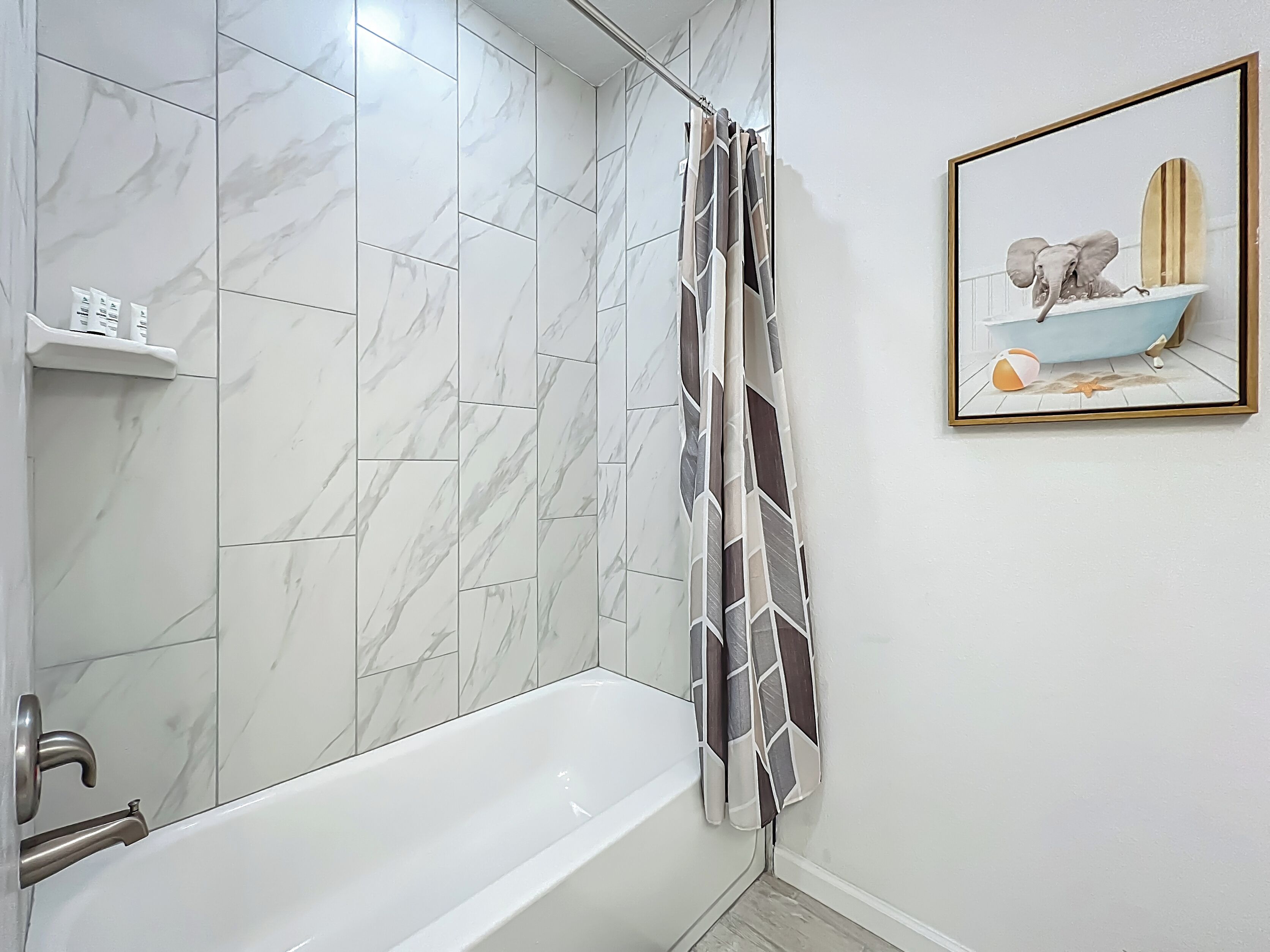 Une salle de bain avec une baignoire blanche, une douche avec un rideau à motifs et une étagère contenant des articles de toilette.
