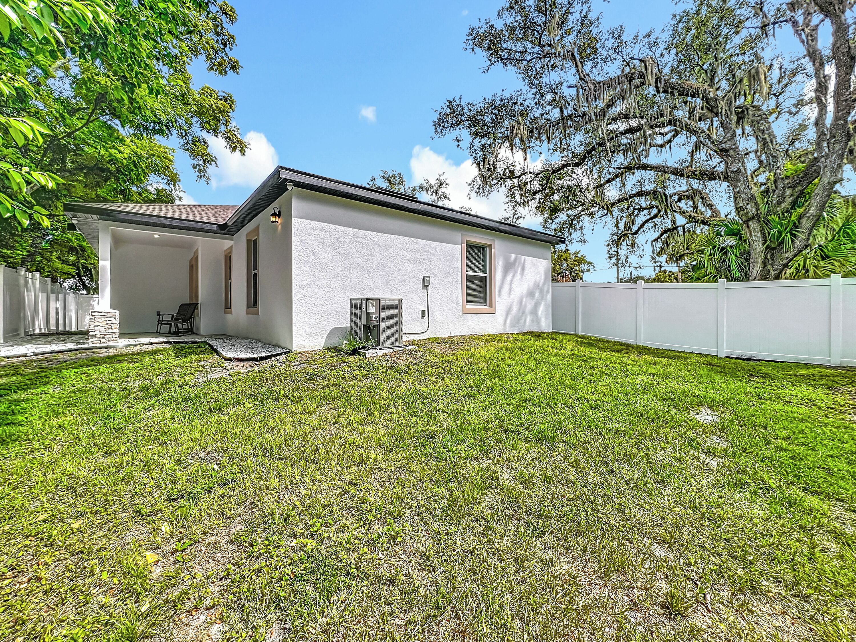 A single-story house with a white exterior, a small front porch with a chair, and a white fence surrounding the property.