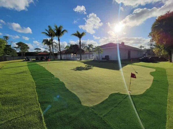 A golf course with a flag, palm trees, and a building in the background.