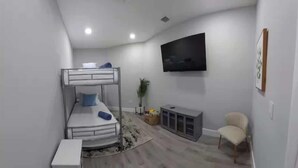 A compact room with bunk beds, a flat-screen TV, a cabinet, and a chair. - 9BR/5BA/Pool/Jacuzzi/Theater/Mini Golf/Beach (Pompano Beach)