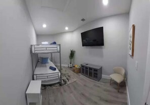 Habitación pequeña con literas, televisión de pantalla plana, armario y una silla.