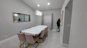 A modern dining area with a long table, pink chairs, and a chandelier.
