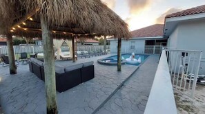 Un área de piscina con sillones reclinables, un pabellón de techo de paja y una piscina.