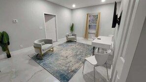A modern room with a white door, a white chair, a small table, and a blue patterned rug.
