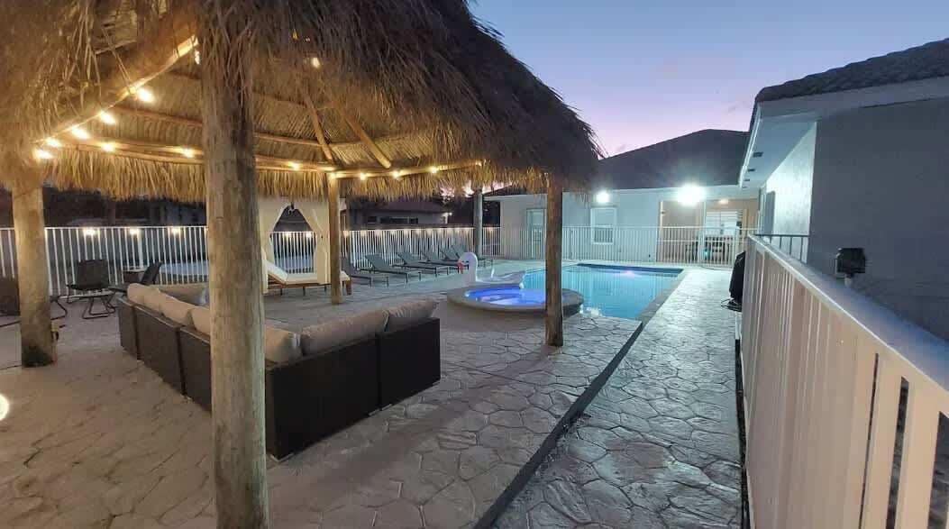 An outdoor pool area with a thatched roof, lounge chairs, and a hot tub.