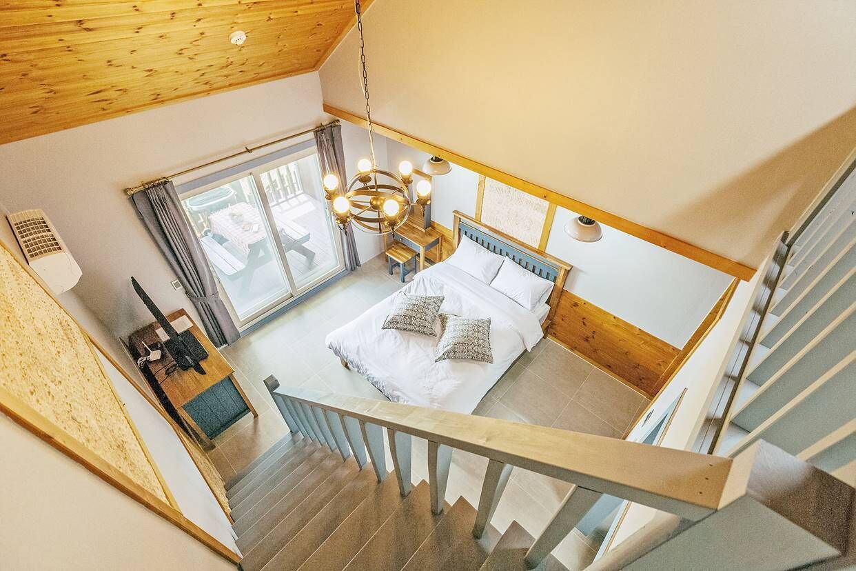 A bedroom with a bed, a chandelier, a window, and a staircase.