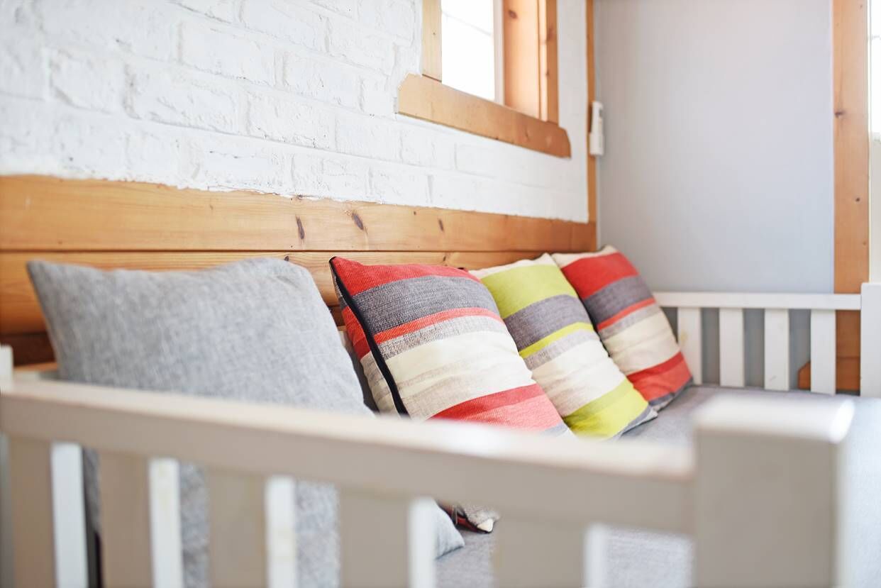 A white crib with a wooden headboard and a white brick wall in the background.