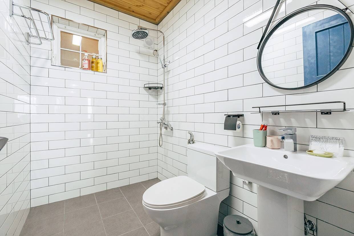 Un bagno moderno con piastrelle bianche stile metro, un water bianco, un lavandino con articoli da toilette e una doccia con porta in vetro.