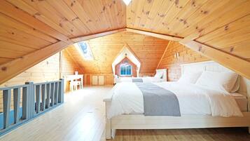 A bedroom with a sloped ceiling, a bed, a small table, and a window.