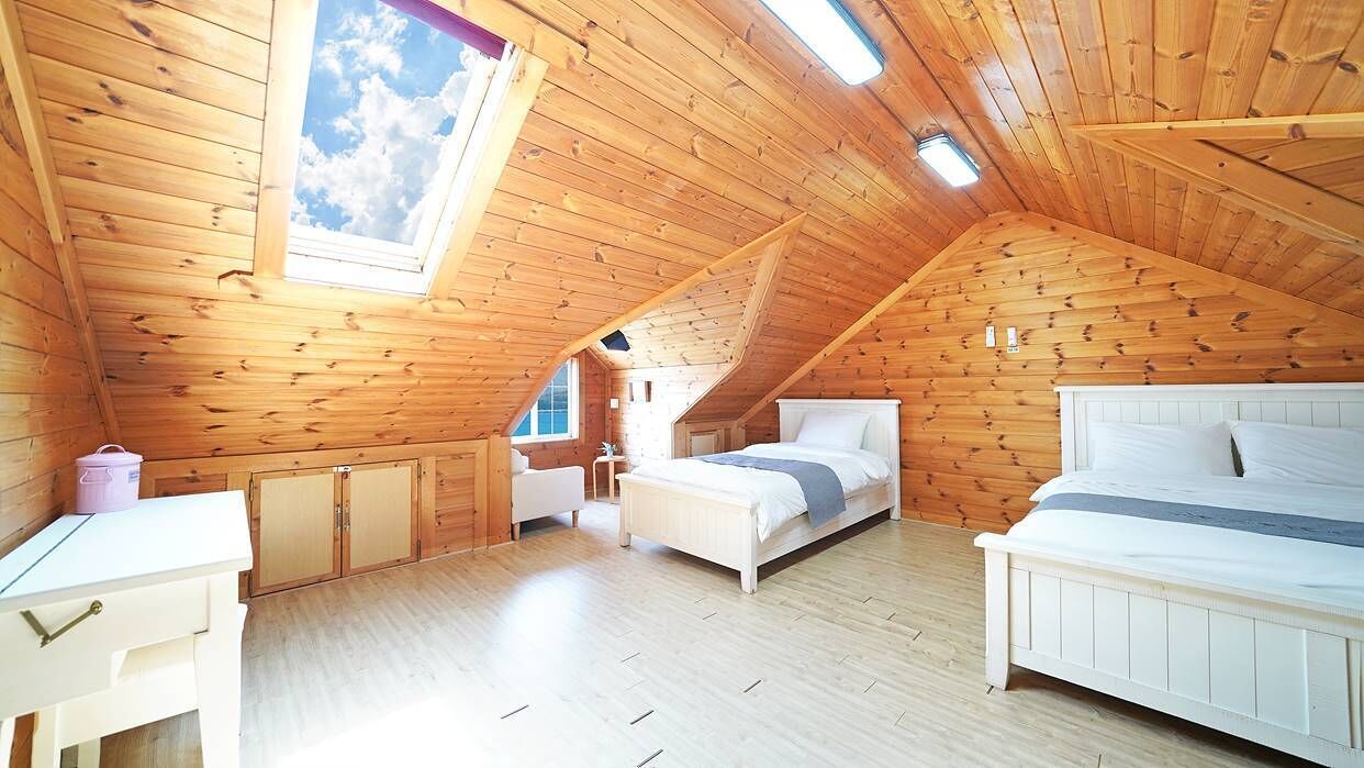 Ein gemütliches Schlafzimmer im Dachgeschoss mit Holzwänden, einem Oberlicht, zwei Betten und einem kleinen Tisch.