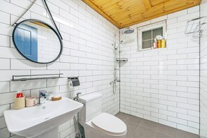 A bathroom with white tiles, a wooden ceiling, a round mirror, a toilet, a sink, and a shower. - SINBIBADA PENSION (Geoje)