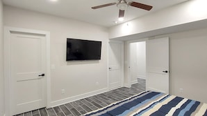 A bedroom with a flat-screen TV mounted on the wall, a ceiling fan, and a striped rug on the floor.