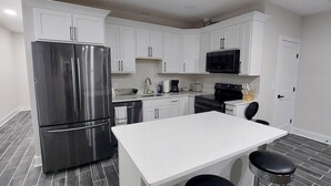 A modern kitchen with white cabinets, a stainless steel refrigerator, a microwave, and a coffee maker.