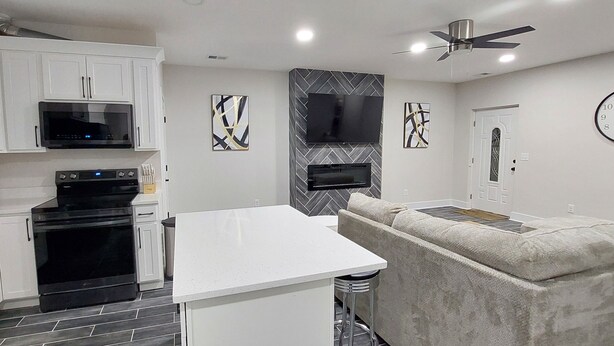 A modern kitchen with white cabinets, a black stove, a microwave, and a flat-screen TV mounted on the wall.
