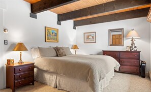 Une chambre avec un grand lit, deux tables de chevet, une commode et un plafond avec des poutres apparentes.