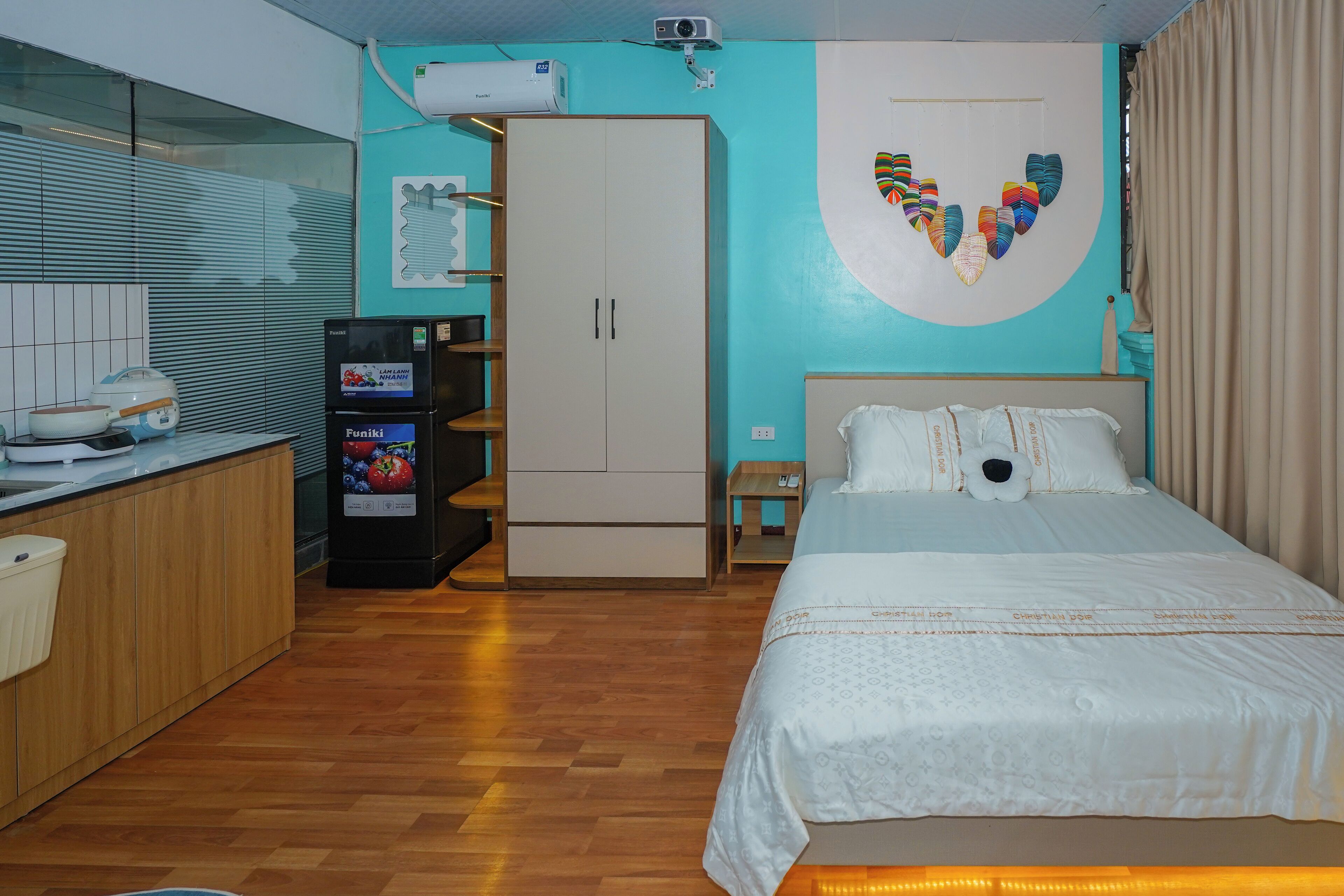 A hotel room with a bed, a wardrobe, a minibar, a wall-mounted air conditioner, and a window with curtains.