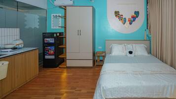 A hotel room with a bed, a wardrobe, a minibar, a wall-mounted air conditioner, and a window with curtains.