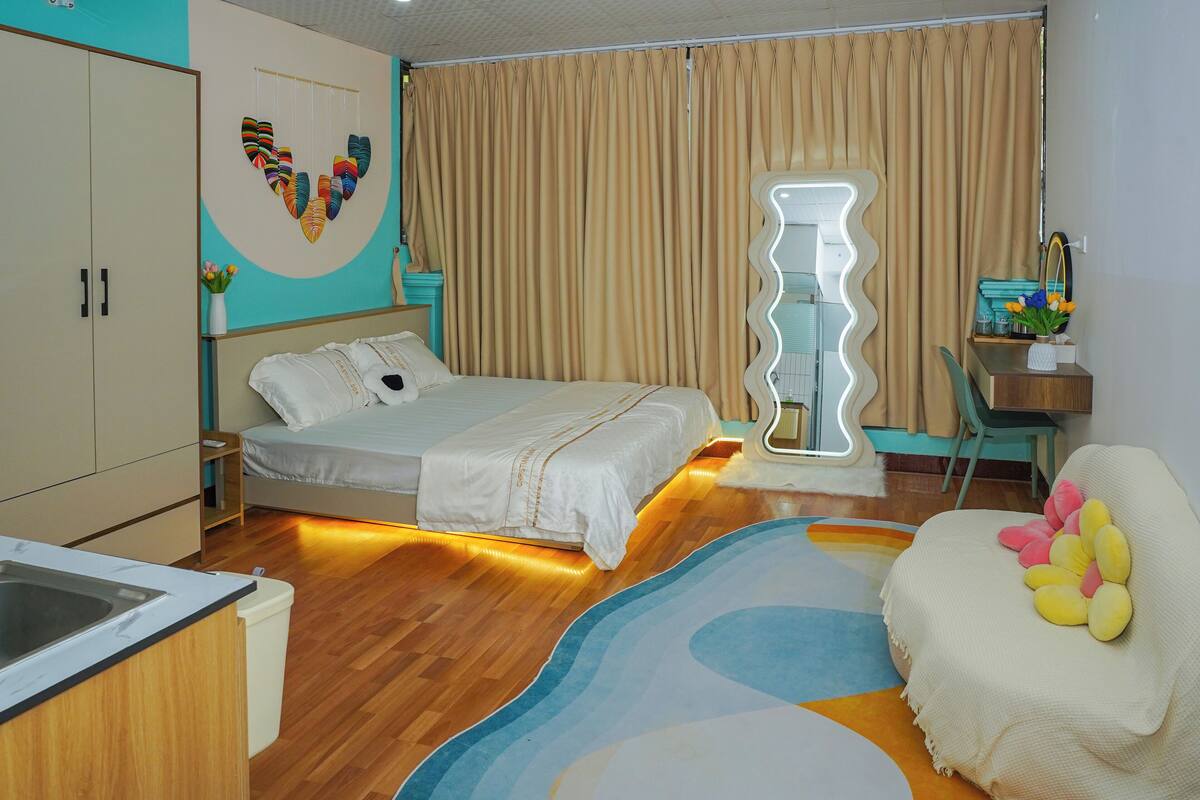 A bedroom with a bed, a desk, a chair, a mirror, and a bathroom.
