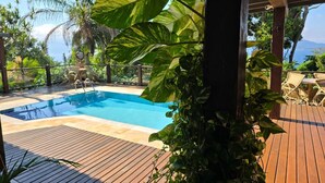 Une piscine dotée d’une terrasse en bois et de chaises longues, entourée d’une végétation luxuriante et de palmiers.