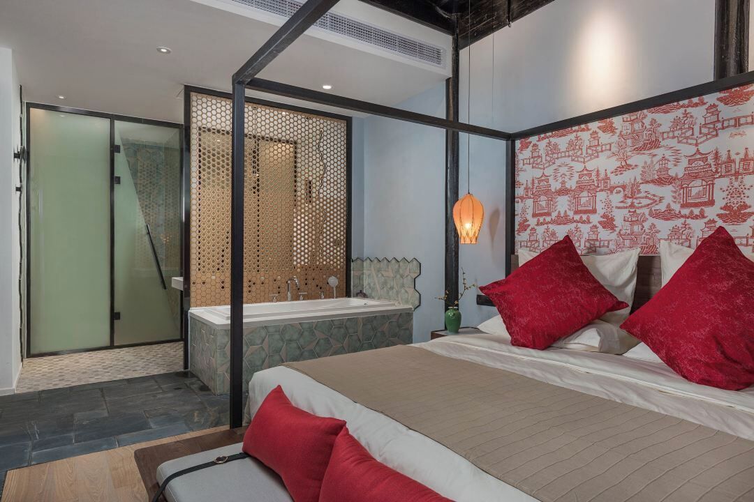 A modern bedroom with a large bed, a glass shower enclosure, and a decorative wall with red patterns.