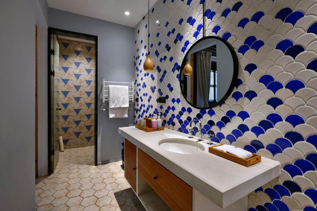 Un baño moderno con un lavamanos blanco, un mueble de madera y una pared de azulejos con diseños azules y blancos.