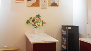 Eine Küche mit weißer Arbeitsplatte, einem schwarzen Kühlschrank, Holzboden und vier gerahmten Kunstwerken an der Wand.