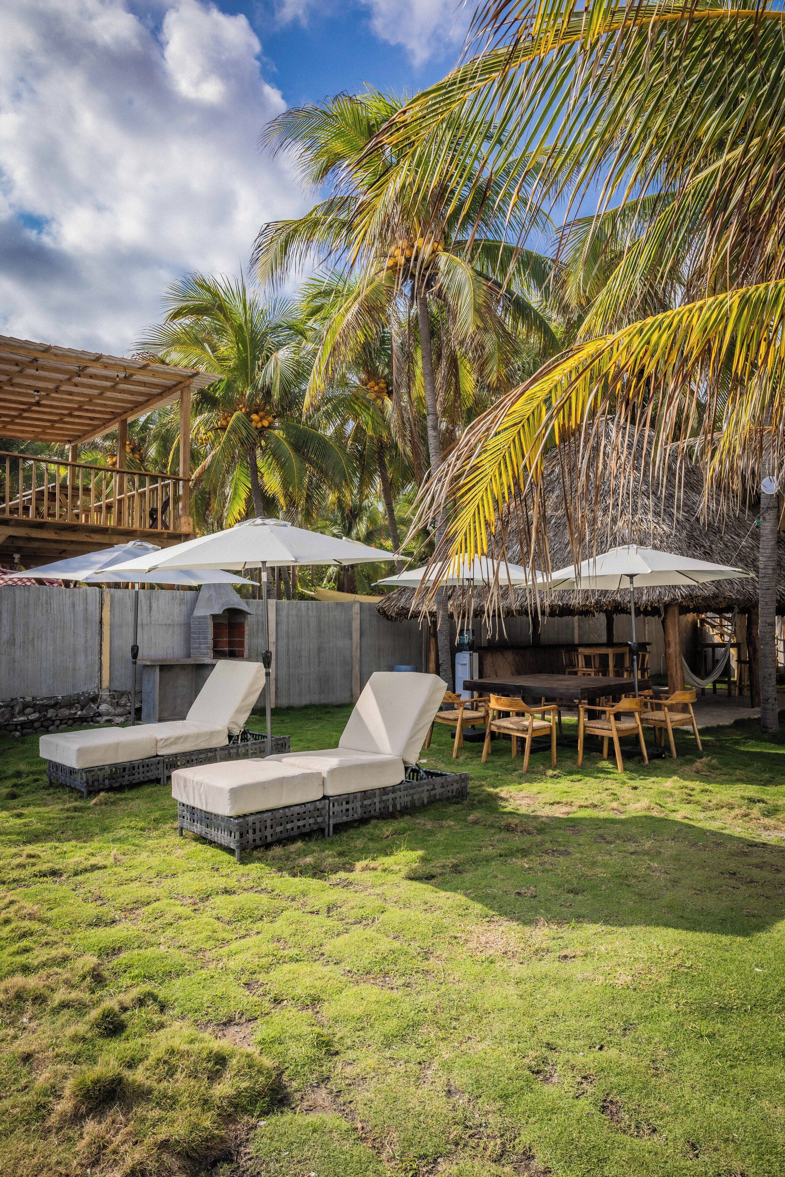A tropical outdoor area with lounge chairs, umbrellas, and a thatched-roof structure.