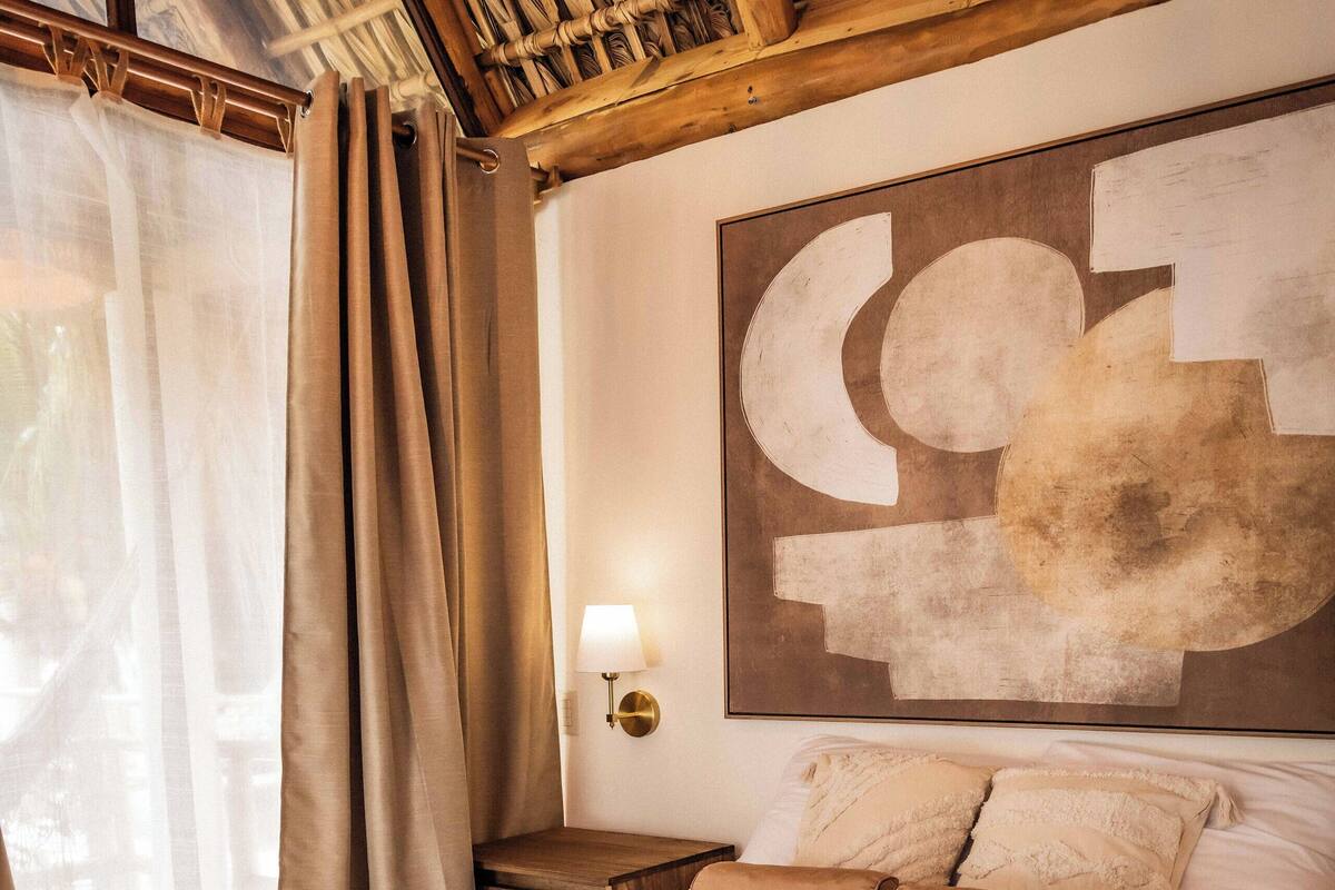 Een slaapkamer met een groot bed, beige gordijnen, een wandlamp en een houten plafond.