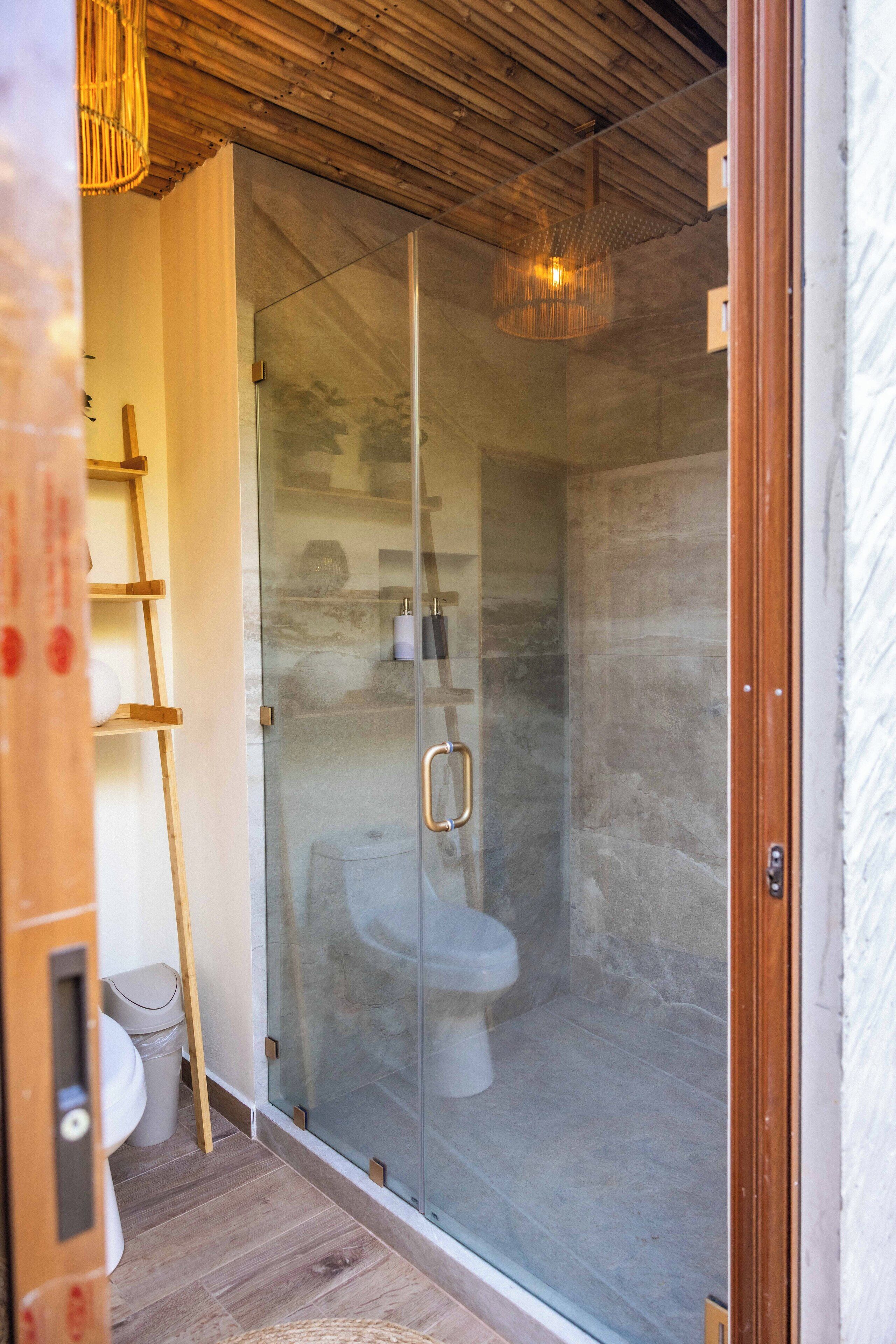 Eine begehbare Dusche mit Glaswänden, Holzboden und einer sichtbaren Toilette durch das Glas hindurch.